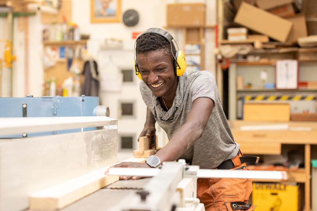 junger dunkelhäutiger Mann mit Gehörschutz schneidet Holz mit Maschine